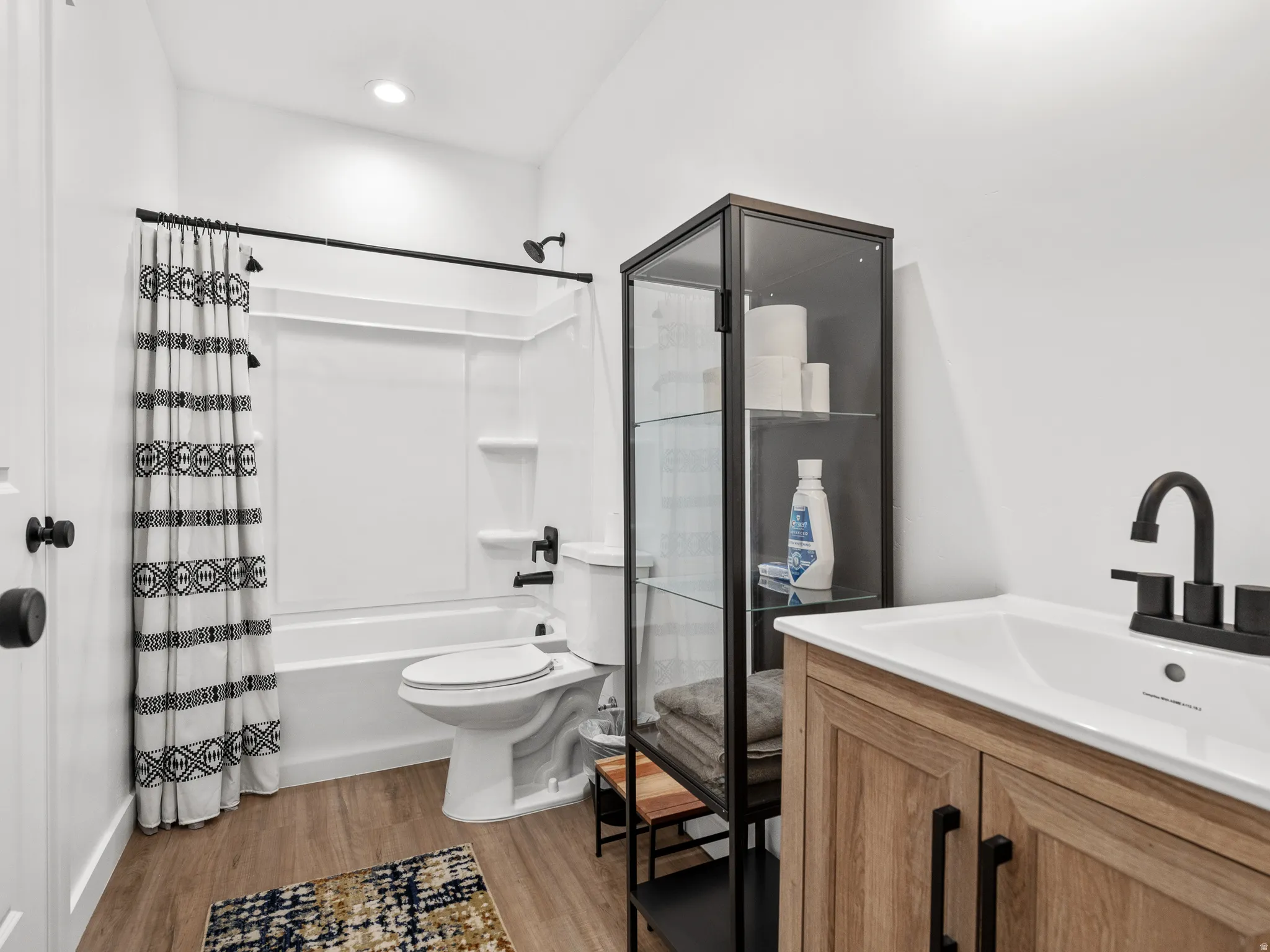 Bathroom featuring a wood-finish vanity with a white countertop sink, matte black faucet, and matching black cabinet hardware