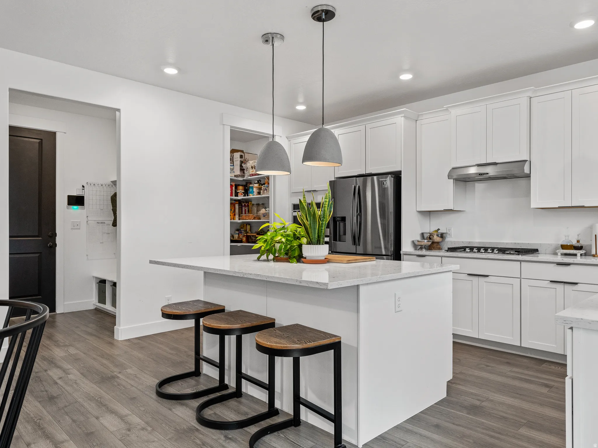 Modern kitchen featuring a central island with countertop seating, white shaker cabinetry, stainless steel appliances, and wood-finish flooring