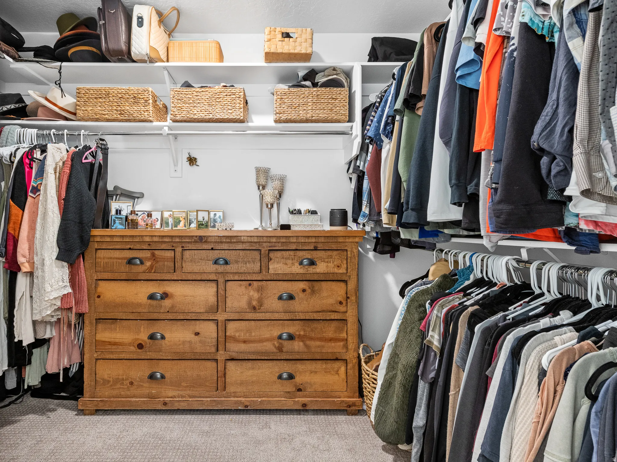 Built-in closet system featuring multiple hanging rods, overhead shelving, and a large wood-finish dresser with drawer storage