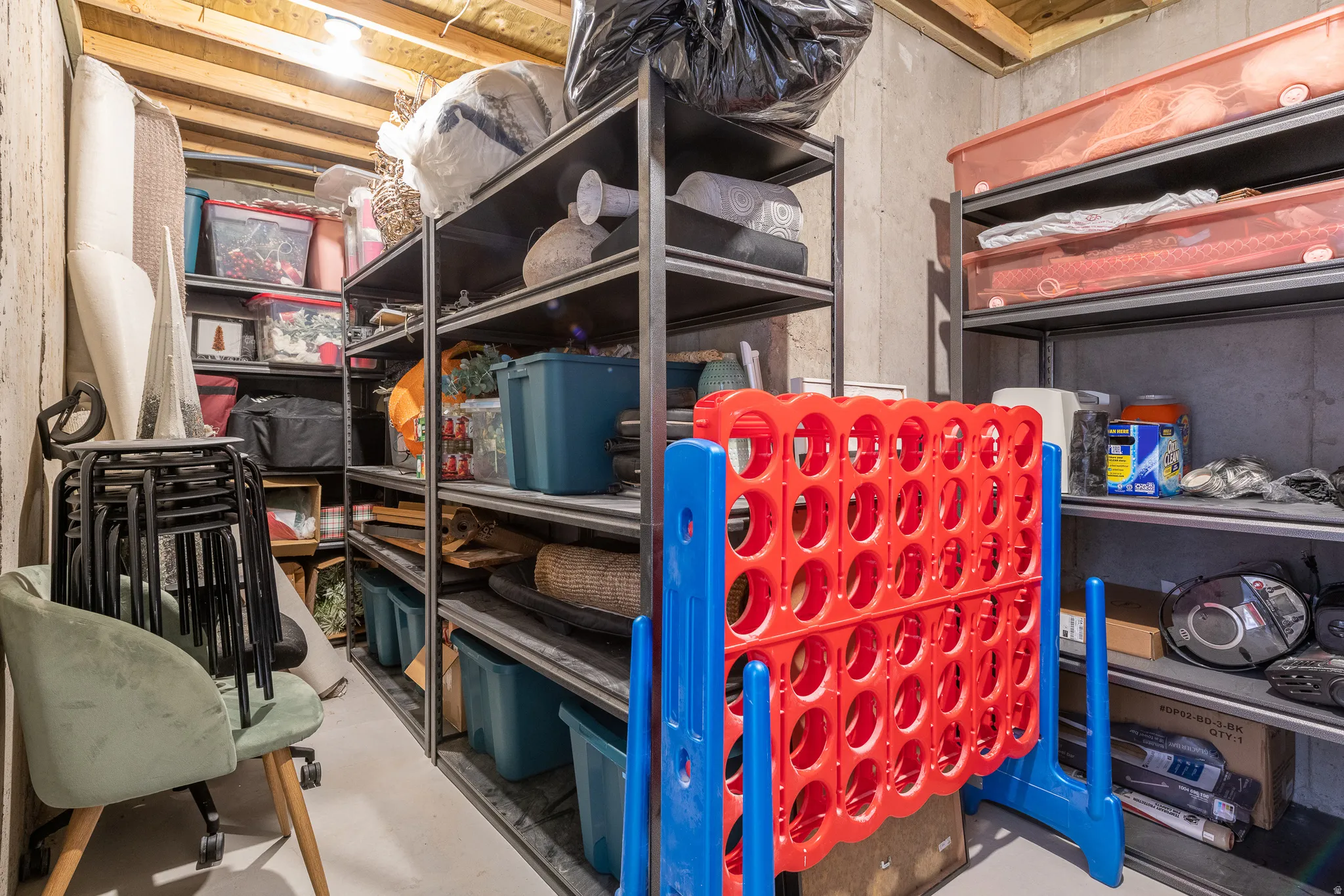 Basement storage area featuring exposed ceiling joists, concrete walls, and overhead lighting
