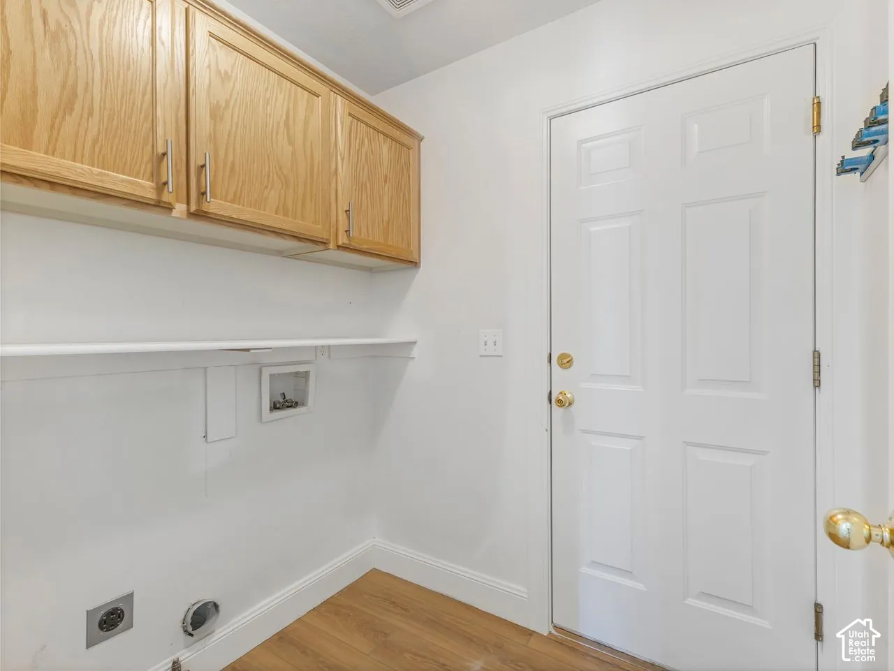 Utility area featuring wood-finish flooring, white walls, and a multi-panel door with brass hardware