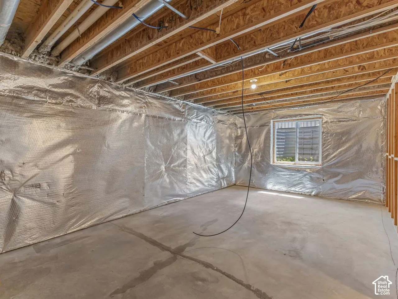 Unfinished basement space featuring a concrete floor, exposed wood ceiling joists, and a window with louvered blinds