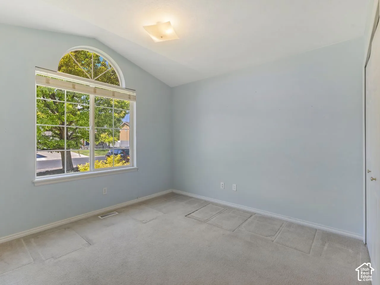 Vaulted ceiling room featuring a large window with an arched transom, light-colored carpeting, a surface-mounted ceiling light fixture, and light blue wall paint