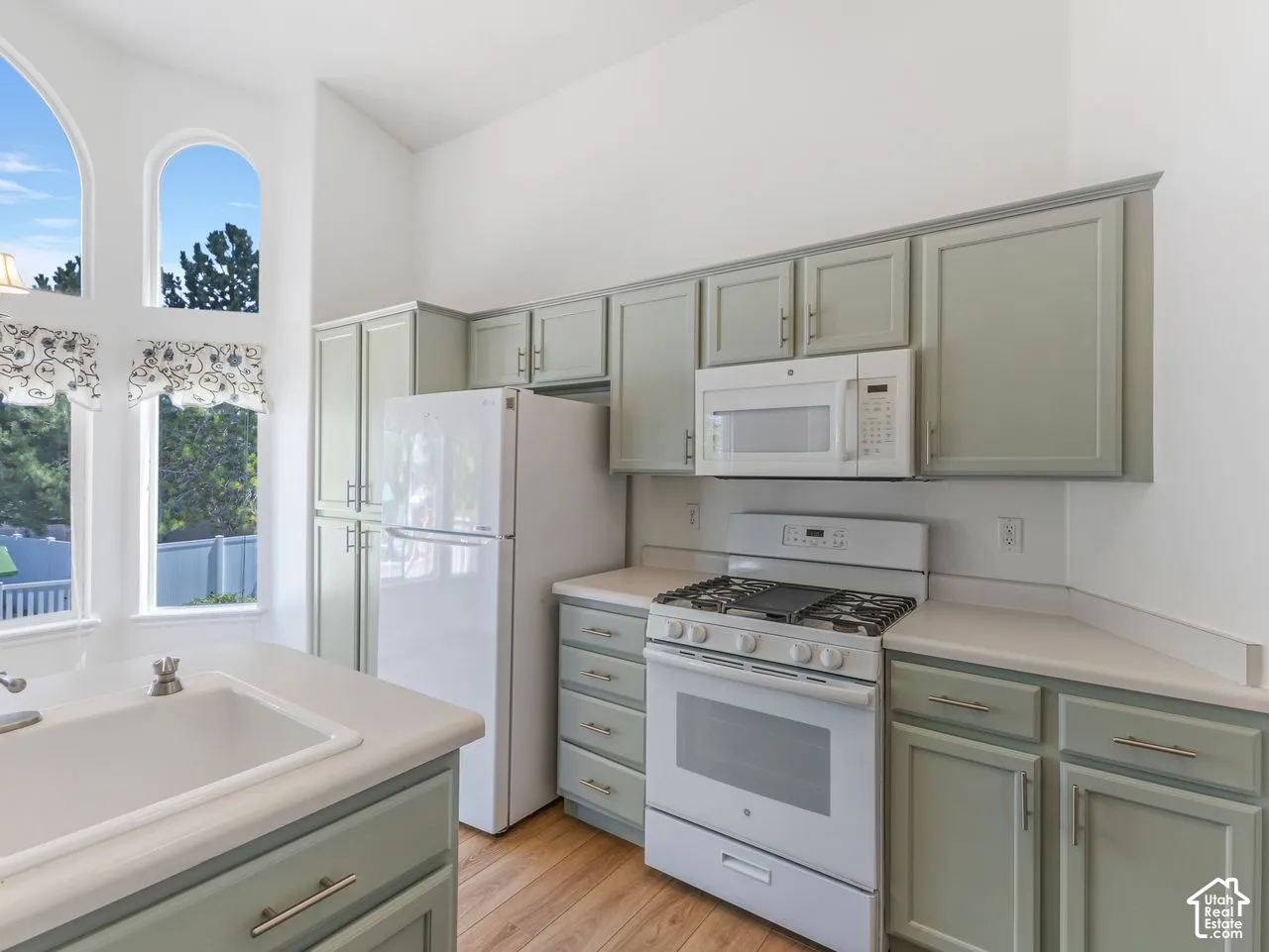 Kitchen featuring light green cabinetry, white appliances, and light-tone countertops