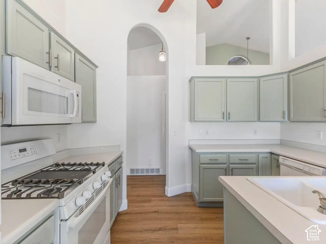 Kitchen featuring light green cabinetry, white countertops, built-in microwave, gas range, and wood-finish flooring