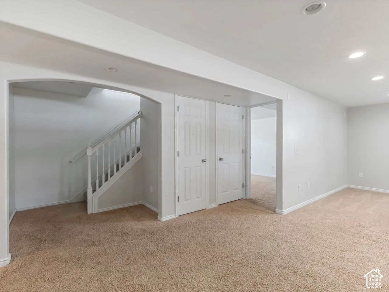 Carpeted living area featuring an arched doorway, white interior doors, a staircase with white railings, and recessed lighting