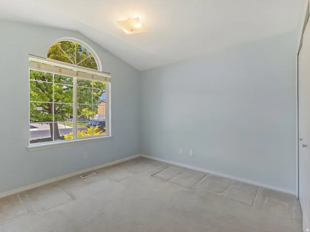Vaulted ceiling room featuring a large window with an arched transom, light-colored carpeting, a surface-mounted ceiling light fixture, and light blue wall paint