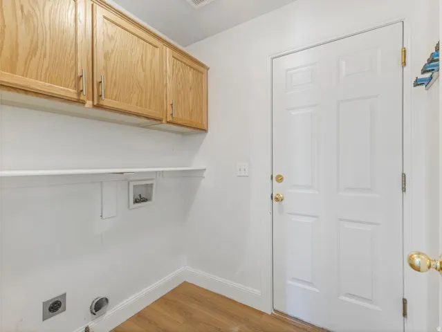 Utility area featuring wood-finish flooring, white walls, and a multi-panel door with brass hardware