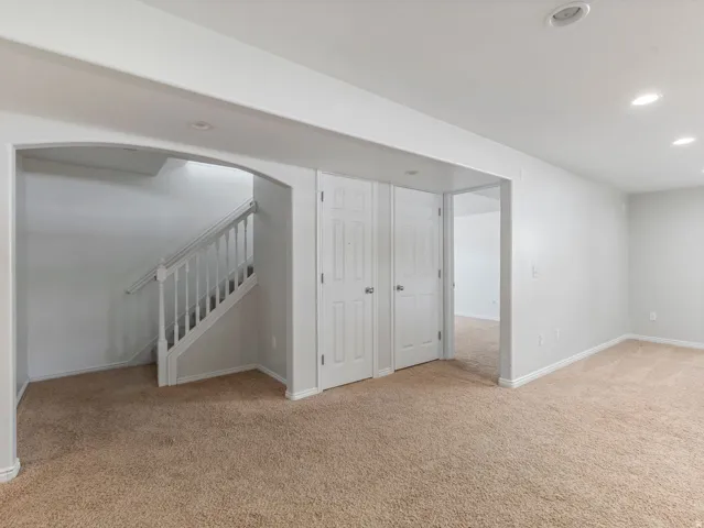 Carpeted living area featuring an arched doorway, white interior doors, a staircase with white railings, and recessed lighting