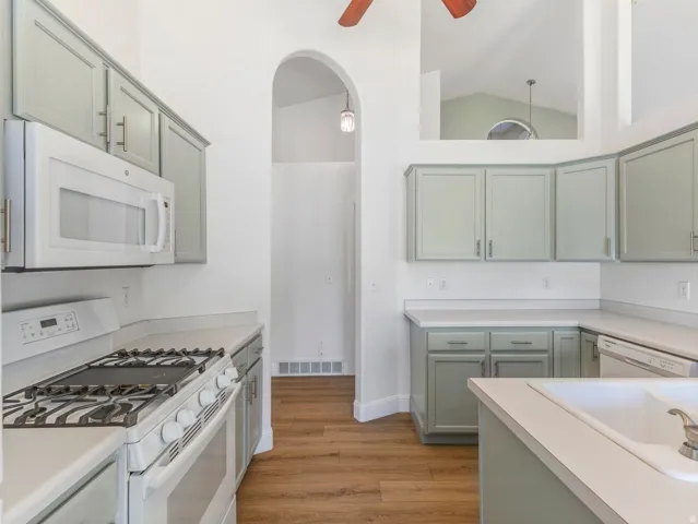 Kitchen featuring light green cabinetry, white countertops, built-in microwave, gas range, and wood-finish flooring