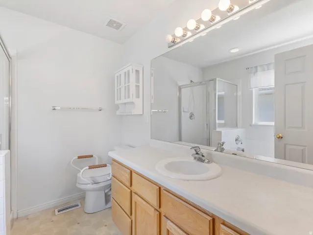 Bathroom featuring a single vanity with wood-finish cabinetry, a large wall-mounted mirror with overhead lighting, a glass-enclosed shower, and a separate bathtub