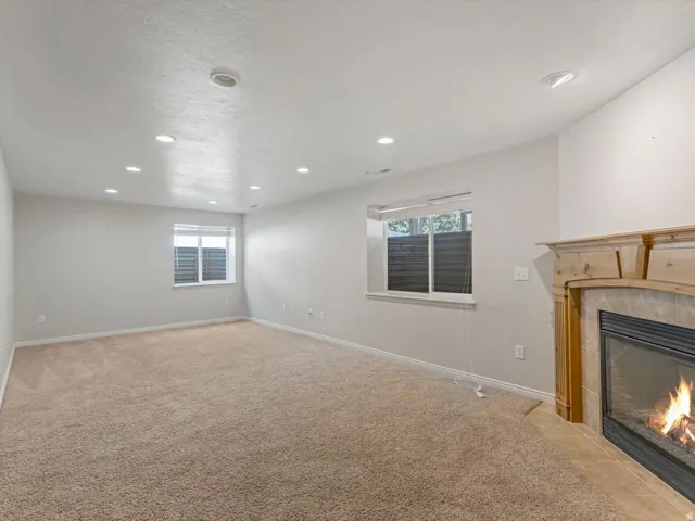 Spacious room featuring a fireplace with a light wood mantel, recessed lighting, two windows with blinds, and carpeting throughout