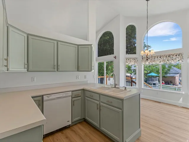 Kitchen featuring custom cabinetry, light-colored countertops, a double basin sink with a gooseneck faucet, a built-in dishwasher, and wood-finish flooring