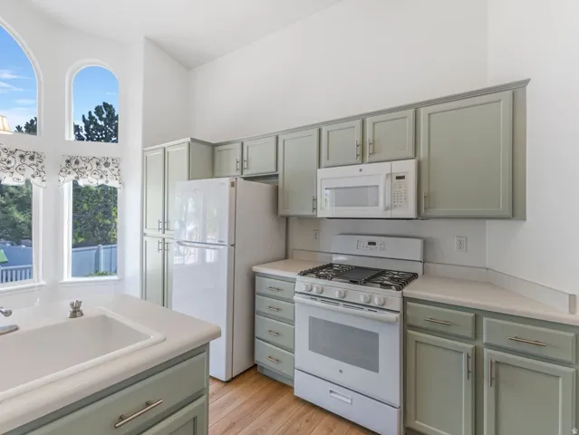 Kitchen featuring light green cabinetry, white appliances, and light-tone countertops