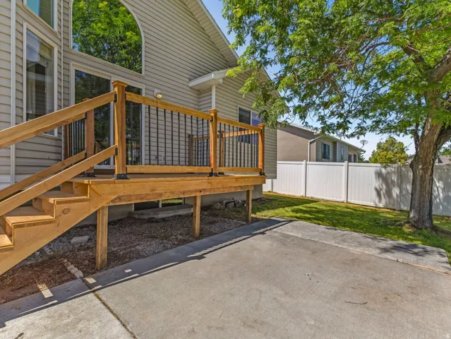 Wood deck with black metal balusters, concrete patio, lawn area, and white privacy fence