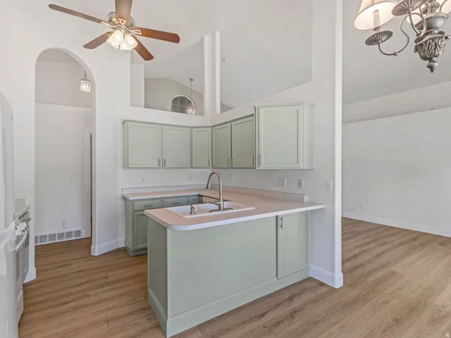 Kitchen featuring wood-finish flooring, light green cabinetry, light-toned countertops, and a stainless steel faucet