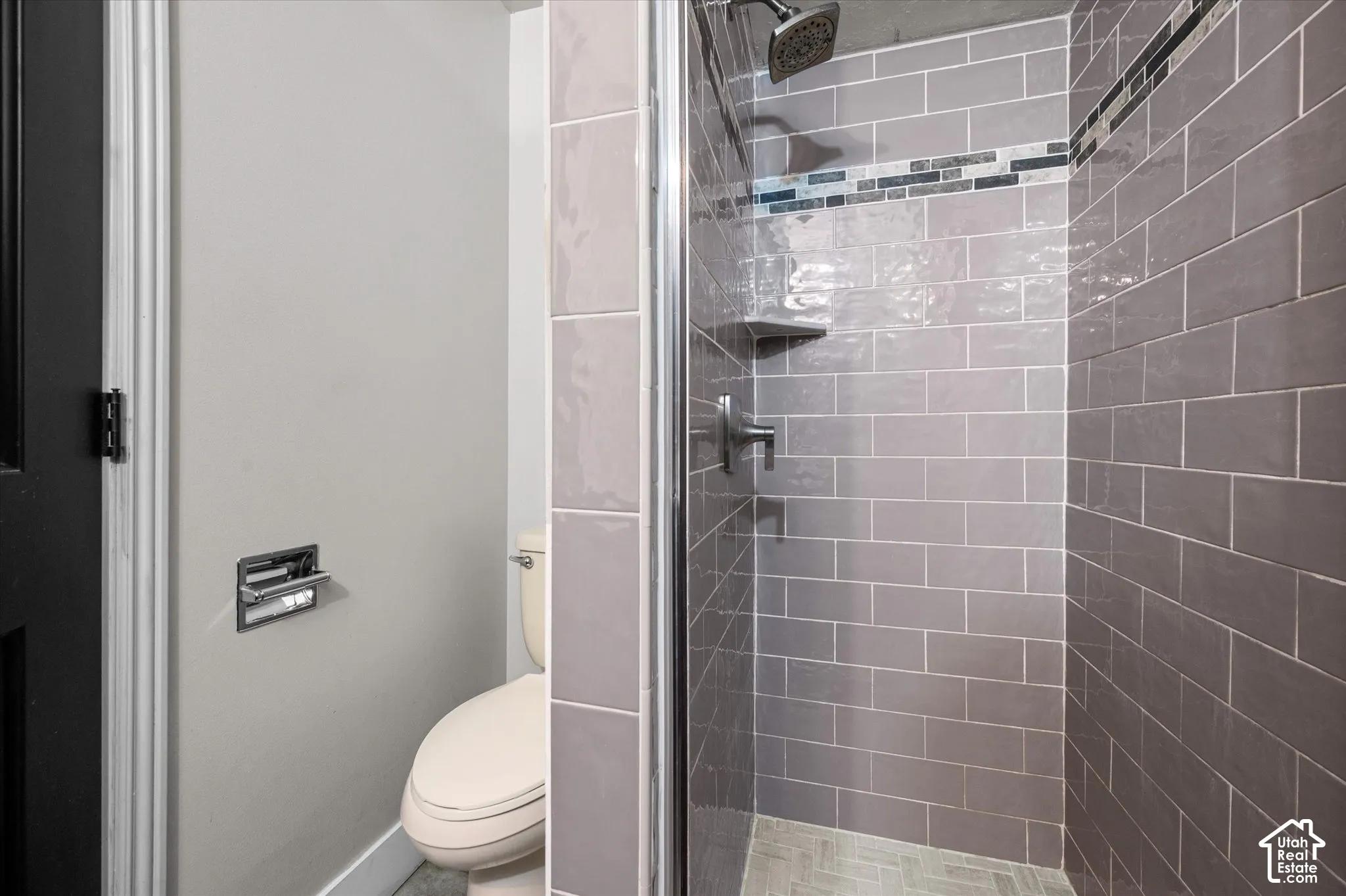 Glass-enclosed shower with gray subway tile surround and a tiled accent band