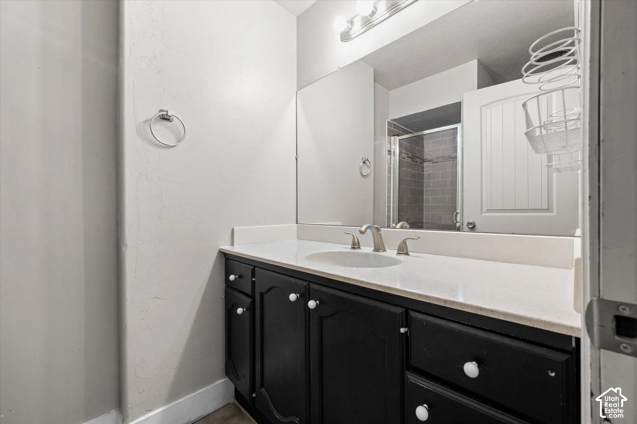 Black vanity with white knobs, white countertop with integrated sink, brushed nickel faucet, and a wall-mounted mirror