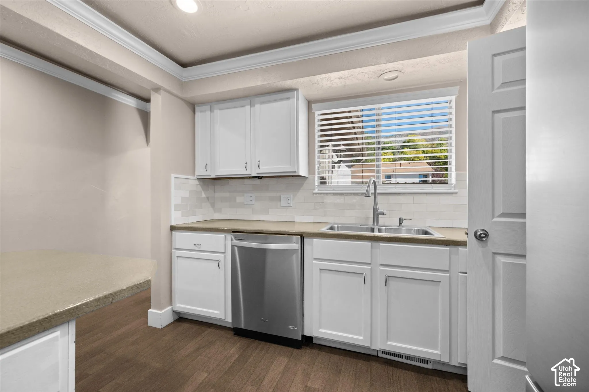 Kitchen featuring white cabinetry, stainless steel dishwasher, undermount sink, and wood-finish flooring