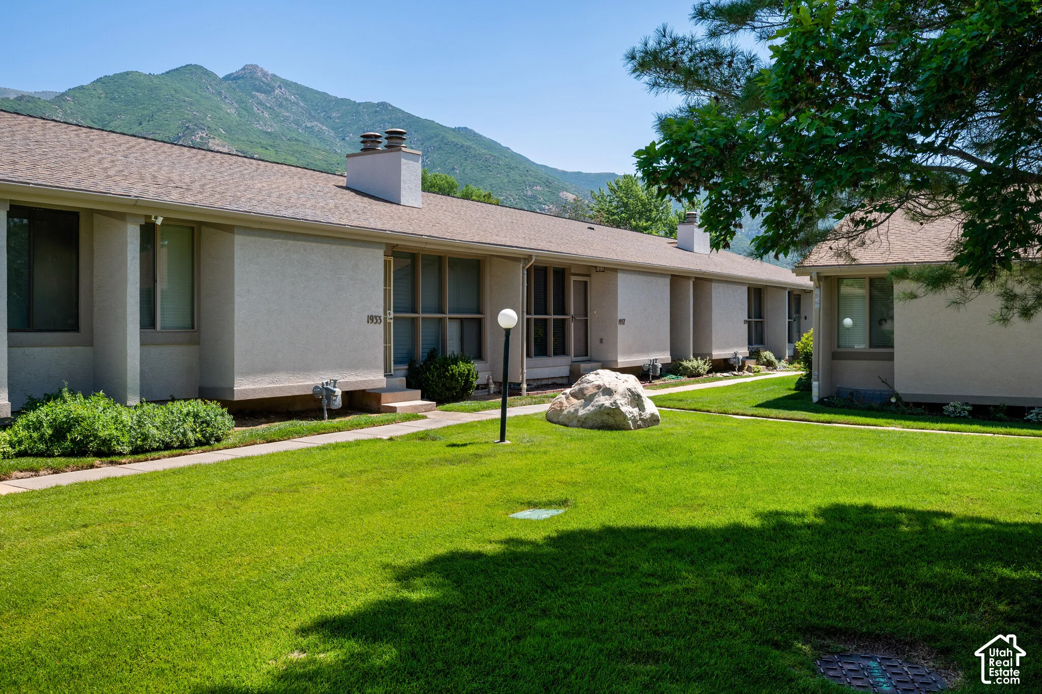 Manicured green lawn with a large decorative boulder and a walkway leading to multiple units