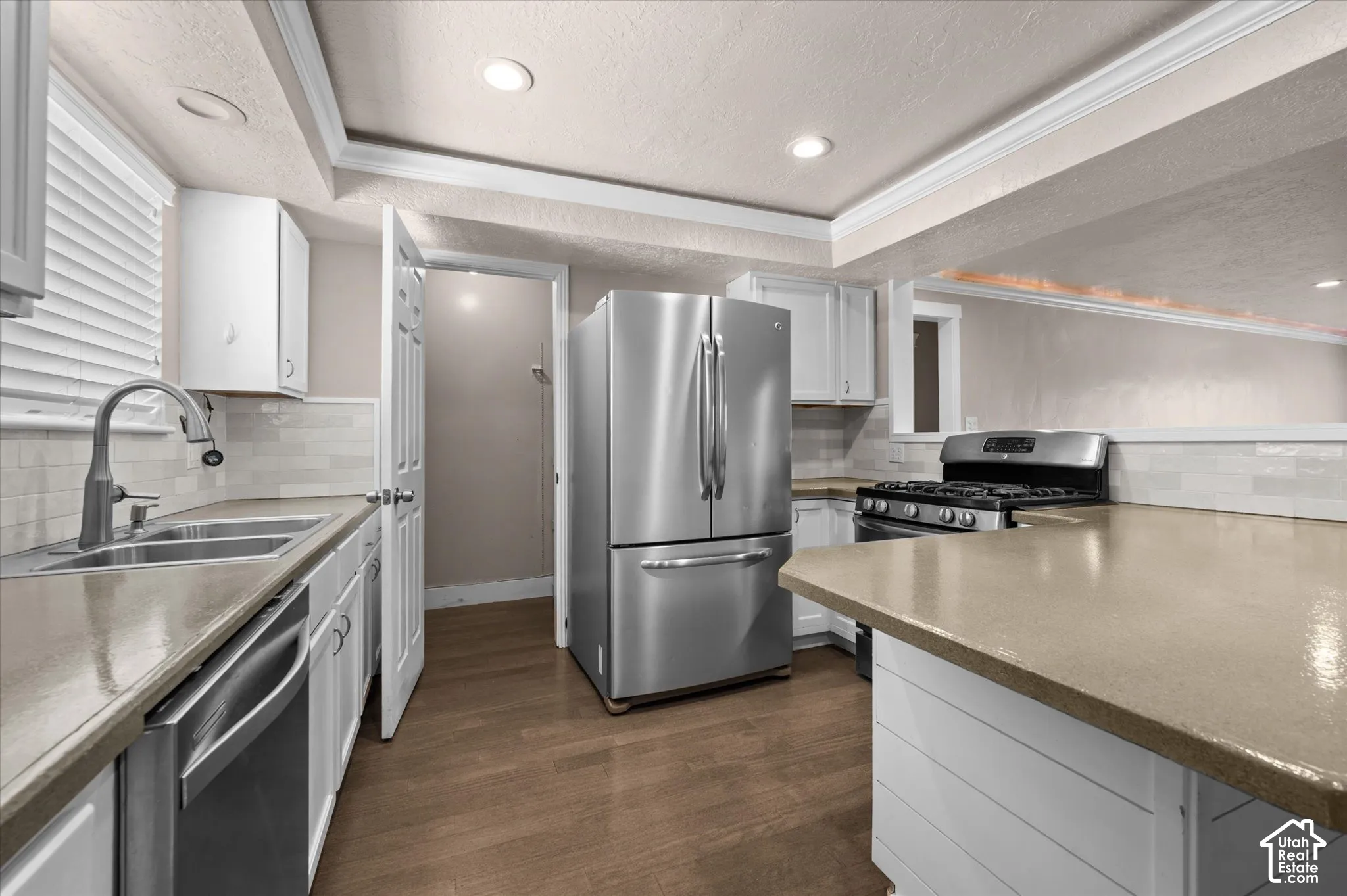 Kitchen featuring wood-finish flooring, stainless steel appliances, white cabinetry, light-toned countertops, and recessed lighting