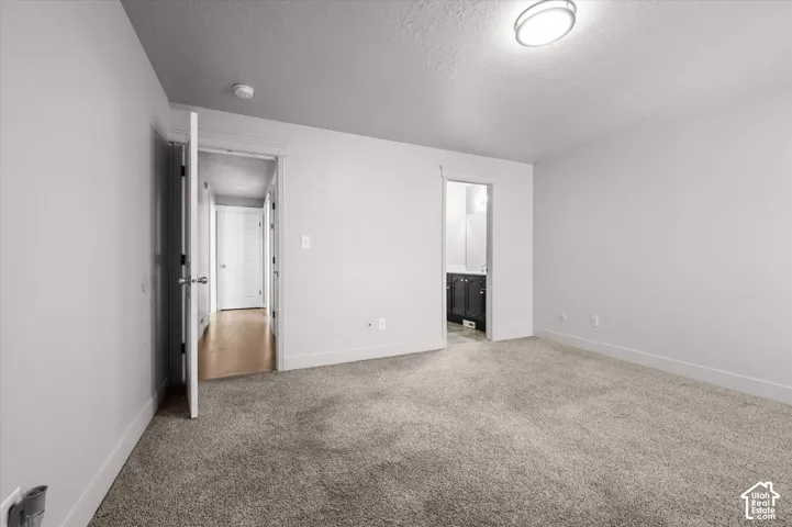 Spacious carpeted bedroom featuring clean white walls, recessed ceiling lighting, and dual mirrored closet doors with frameless hardware