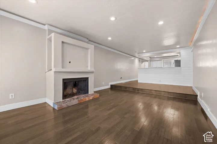 Built-in fireplace with a stone hearth, wood-finish flooring, recessed lighting, crown molding, and a built-in media niche