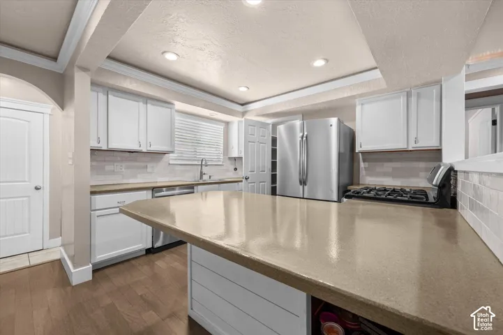 Kitchen featuring an expansive center island, white shaker cabinetry, stainless steel appliances, and wood-finish flooring