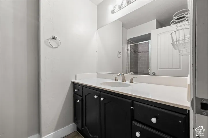 Black vanity with white knobs, white countertop with integrated sink, brushed nickel faucet, and a wall-mounted mirror