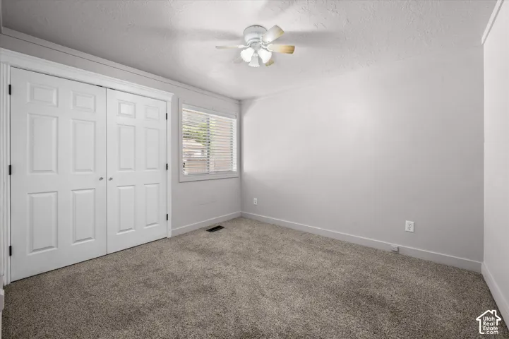 Soft gray carpeting with white trim, a double-door closet, and a ceiling fan with integrated lighting