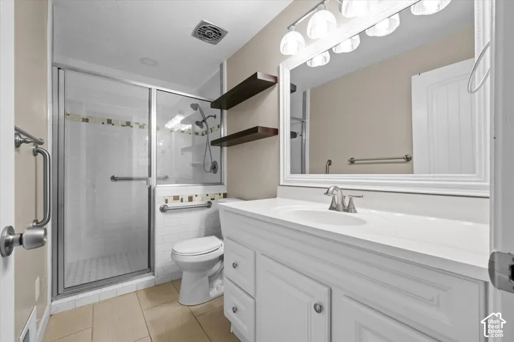 Spa-inspired primary bathroom featuring a frameless glass-enclosed shower with tile surround, dual vanity with white cabinetry and integrated sink, LED-lit mirror, ceramic tile flooring, and recessed ceiling lighting