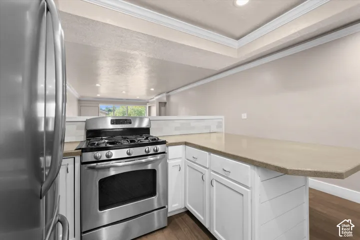 Stainless steel gas range, white cabinetry, light-toned countertops, subway tile backsplash, and wood-finish flooring