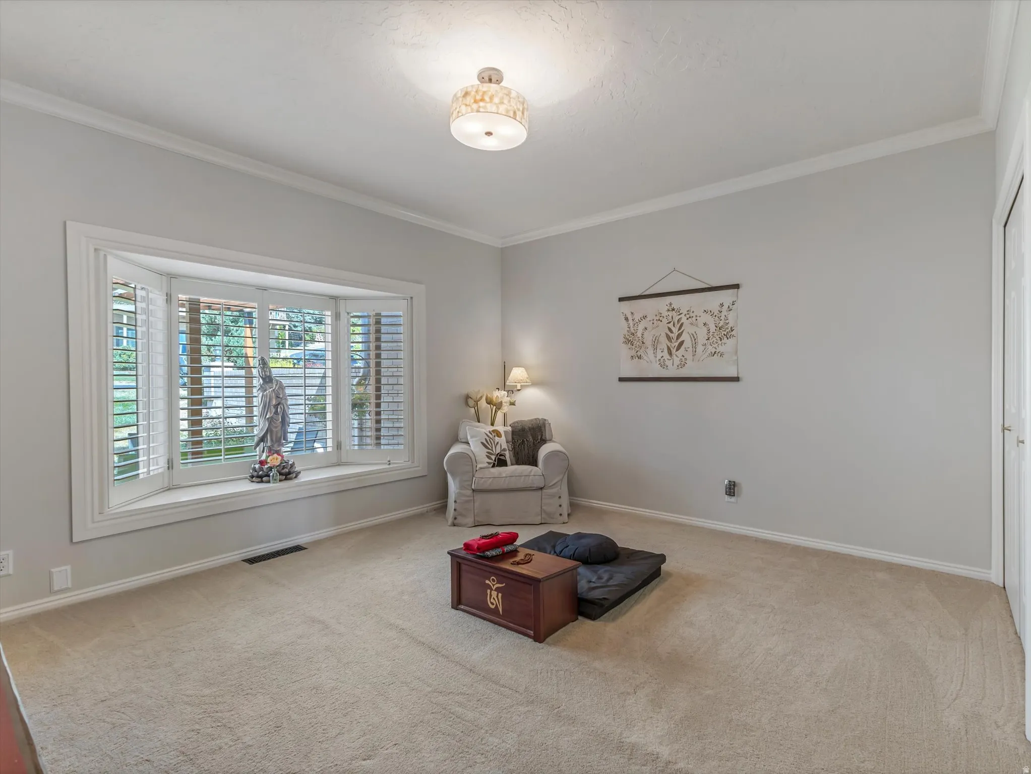 Spacious room featuring a bay window with plantation shutters, light-toned carpeting, crown molding, and a flush mount ceiling fixture