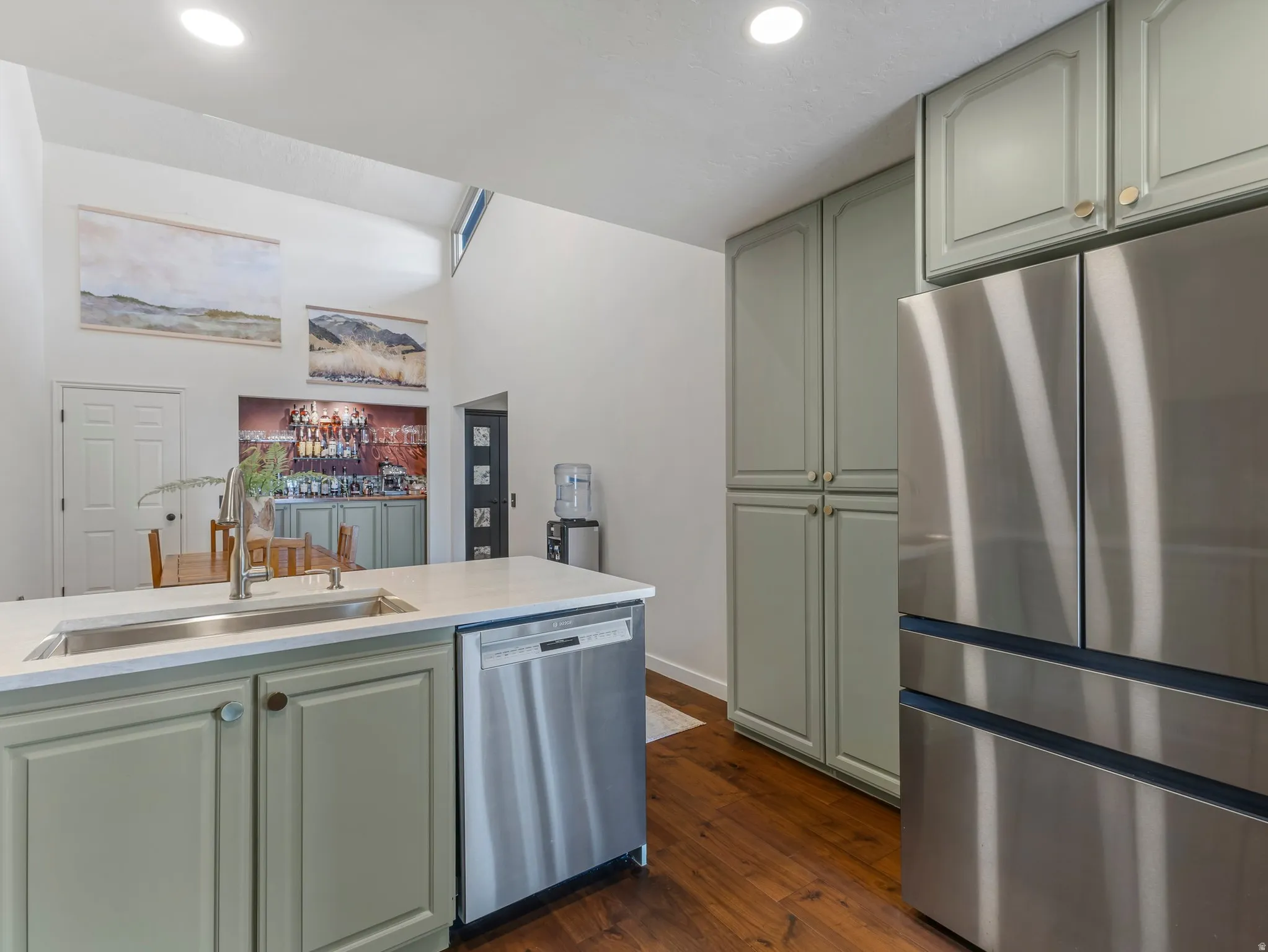 Kitchen featuring light green cabinetry, stainless steel appliances, a white countertop, and wood-finish flooring