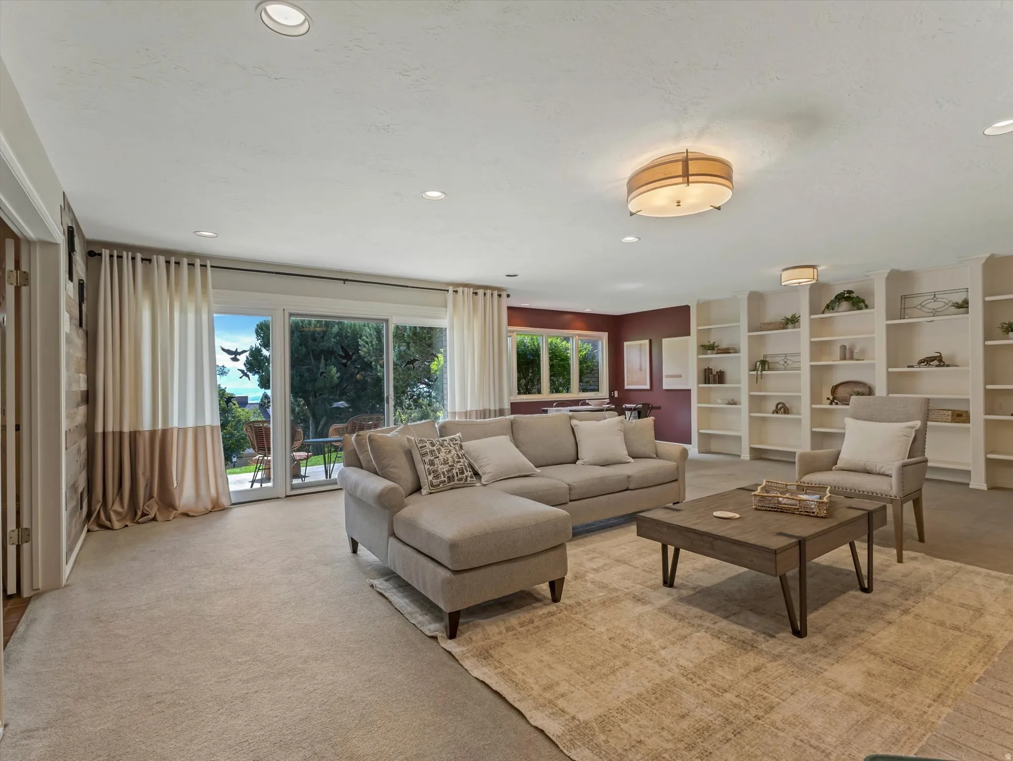 Living area featuring recessed lighting, a built-in wall of shelving, sliding glass doors to the exterior, and neutral carpeting