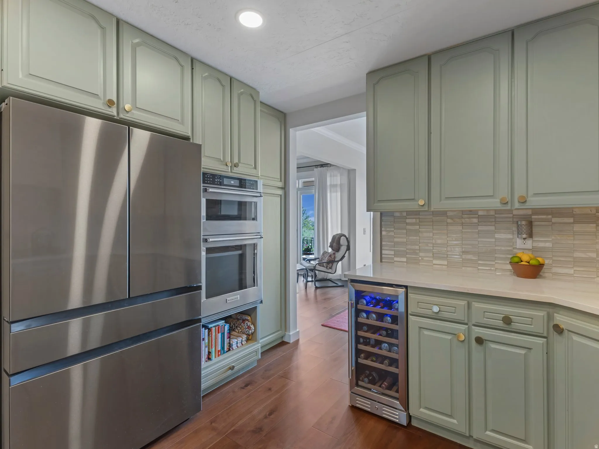 Kitchen featuring stainless steel refrigerator, built-in double oven, paneled cabinetry, light-toned countertops, and wood-finish flooring