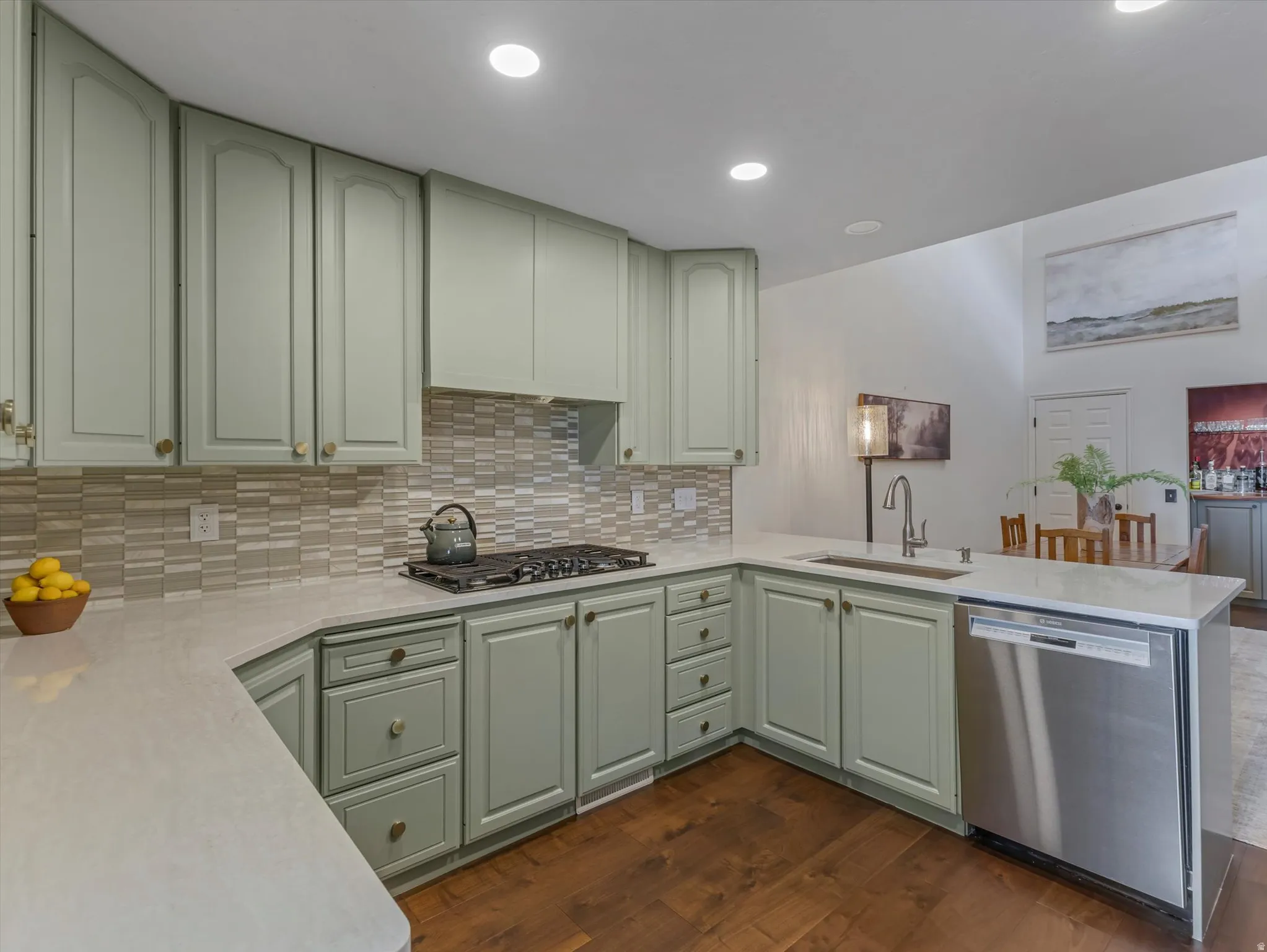 Modern kitchen featuring light green cabinetry, a multi-tone horizontal tile backsplash, and light-colored countertops