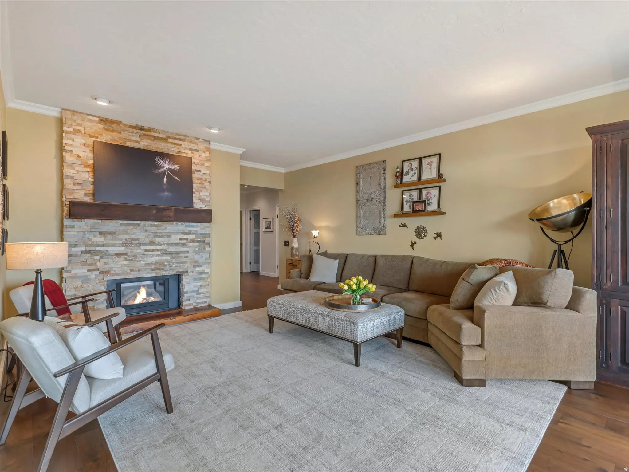 Living area featuring a stone-faced fireplace with a wood-beam mantle, recessed lighting, crown molding, and wood-finish flooring