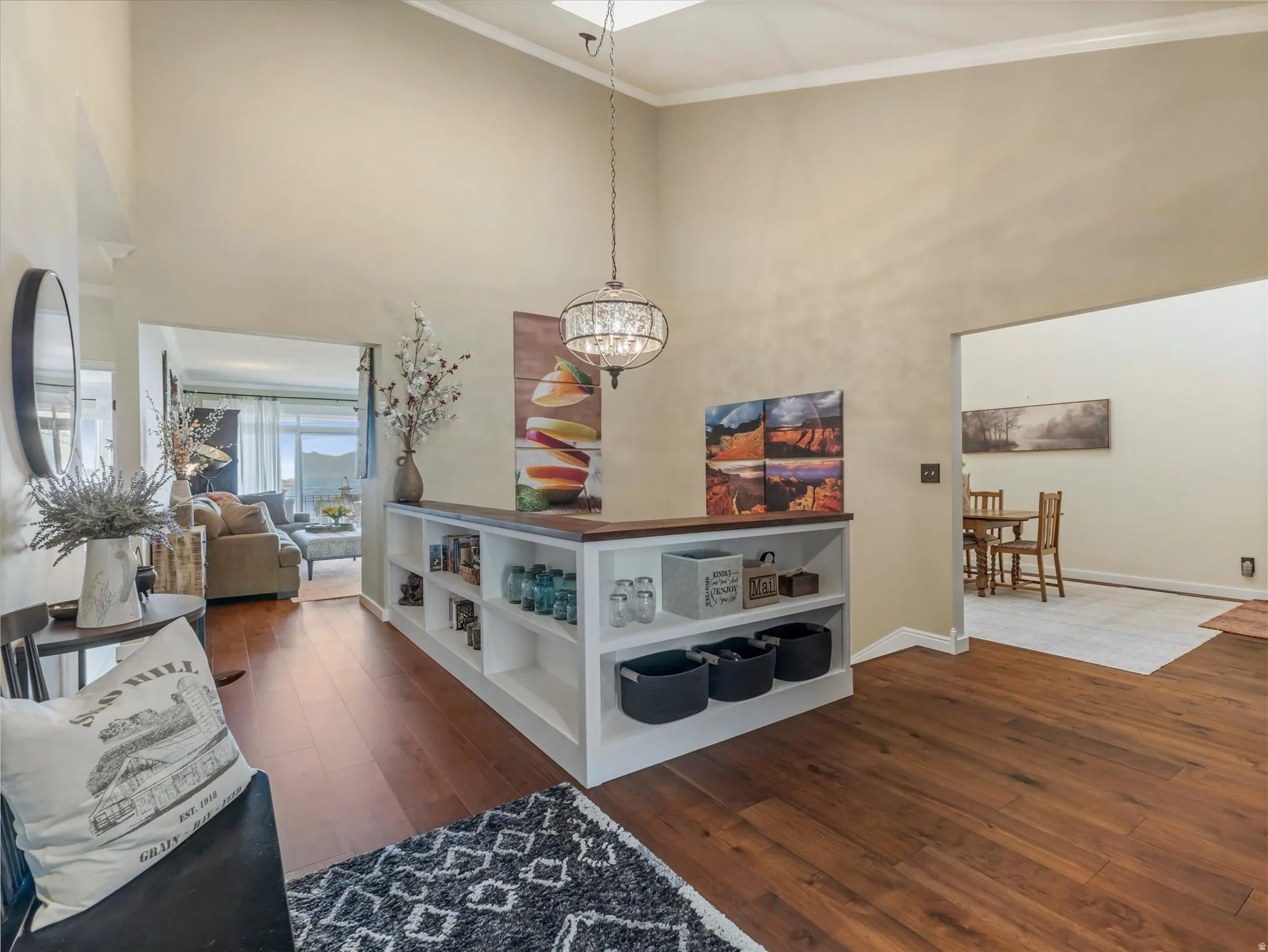 Vaulted ceiling with an elegant chandelier, wood-finish flooring, built-in shelving with a wood top, and open archways to additional spaces