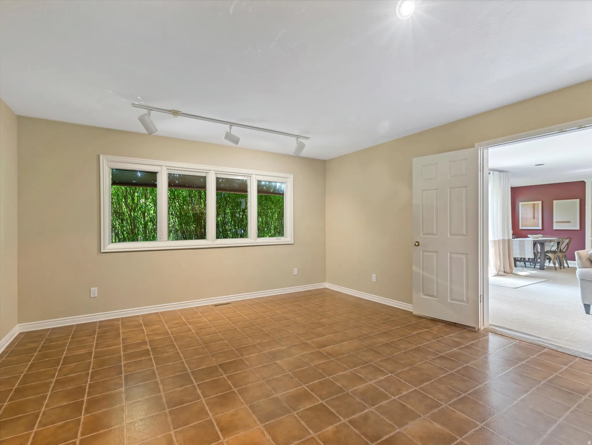 Spacious room featuring terra cotta tile flooring, soft neutral wall finishes, and abundant natural light from four-panel casement windows