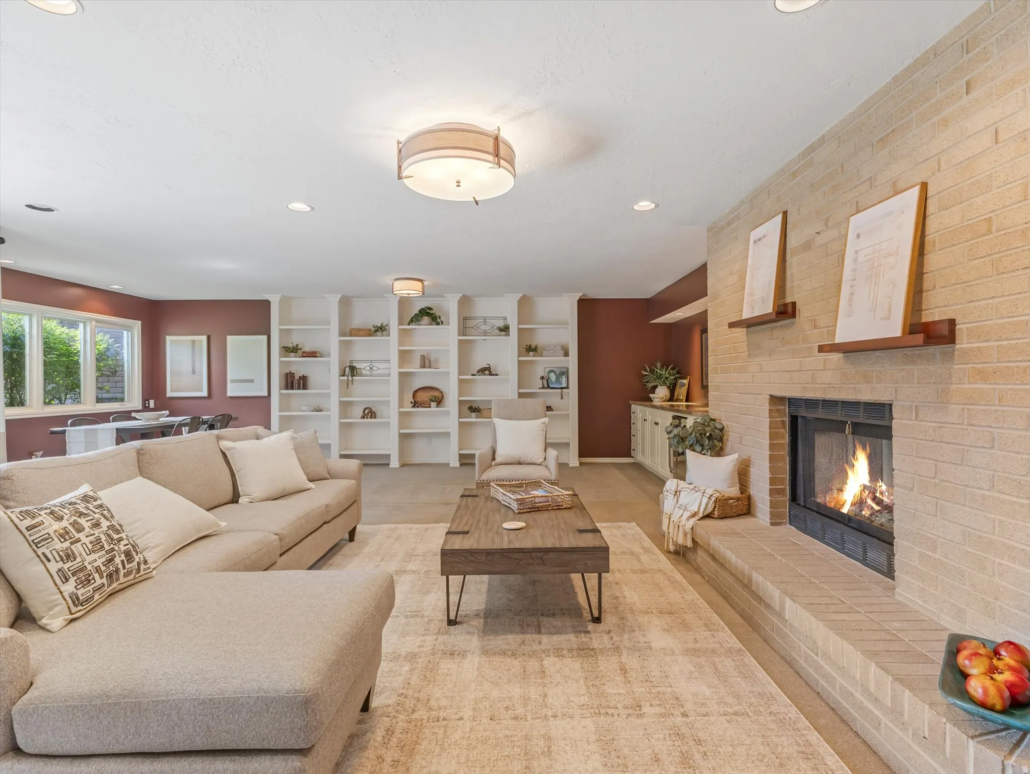 Spacious living area featuring a light-colored brick fireplace with hearth, recessed lighting, built-in shelving, and large windows