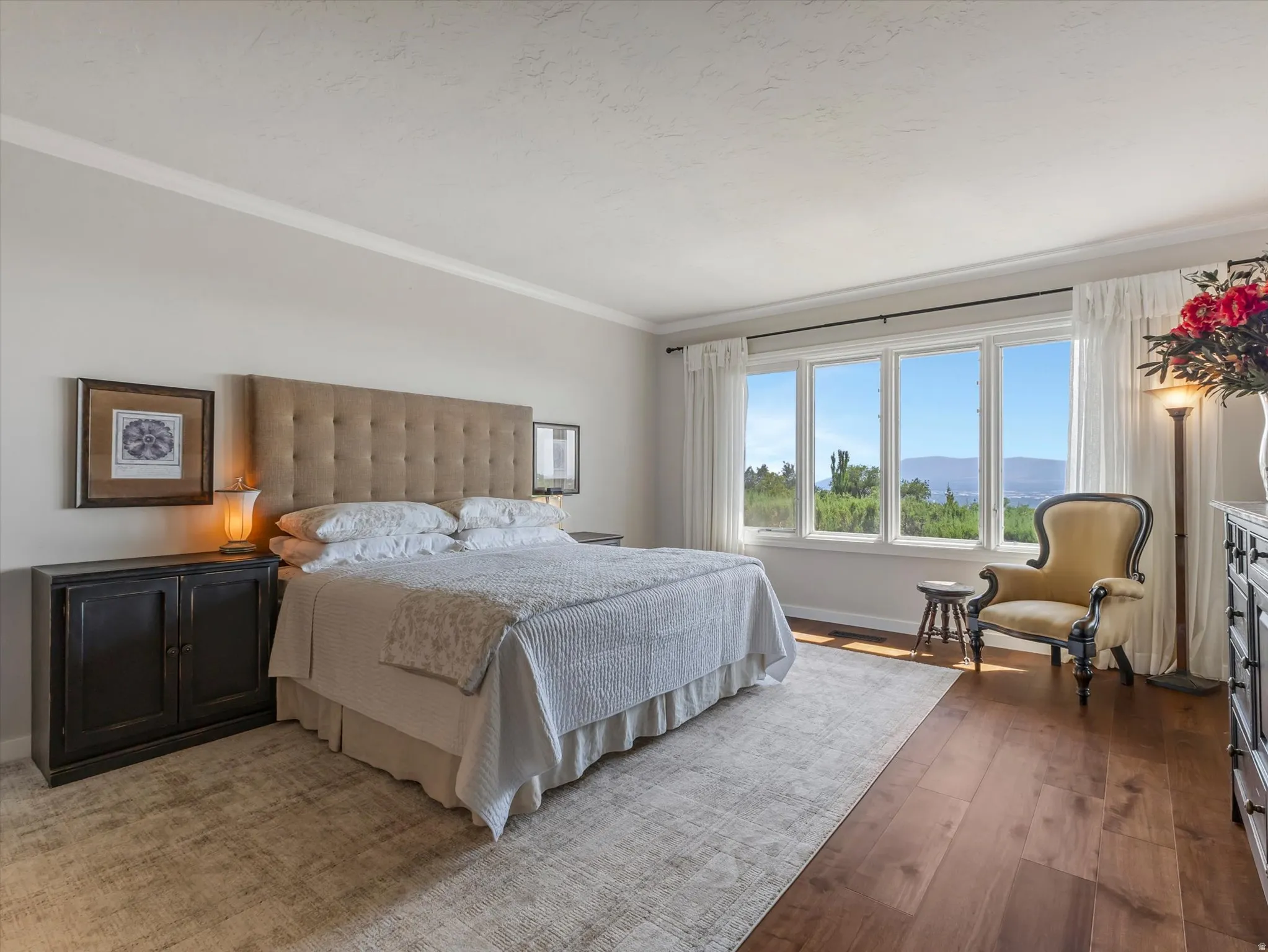 Spacious room featuring wide plank wood-finish flooring, a large multi-pane window with a landscape backdrop, and crown molding
