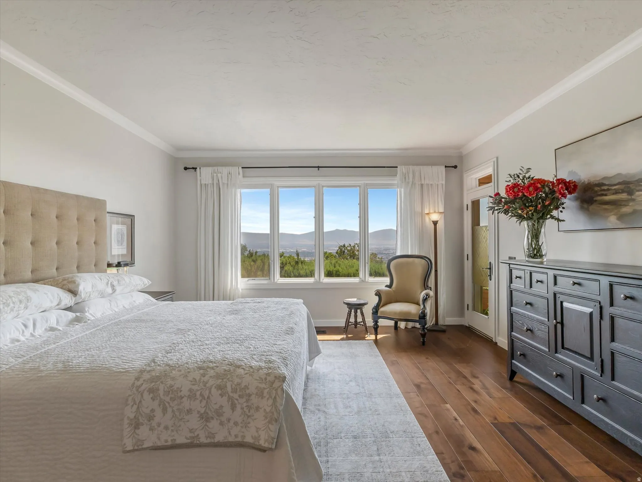 Spacious room featuring wood-finish flooring, a multi-pane window with mountain scenery, and crown molding