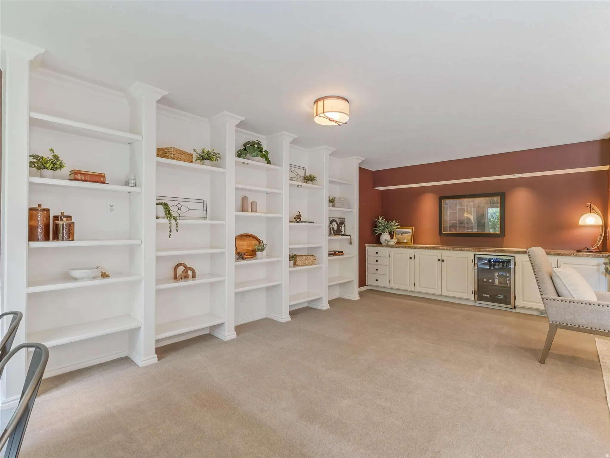 Built-in white shelving units spanning a wall, complemented by a long built-in cabinet system with a beverage refrigerator