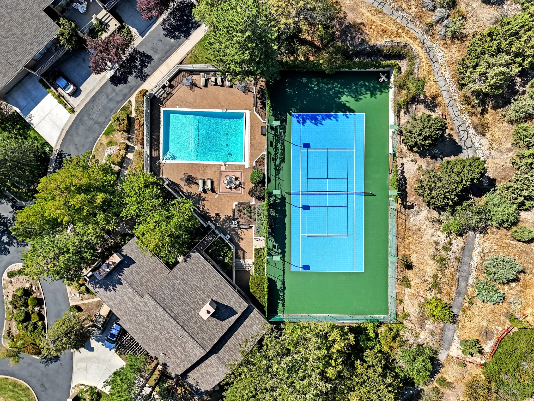 Expansive outdoor area featuring a swimming pool, paved pool deck, tennis court, and surrounding natural landscaping