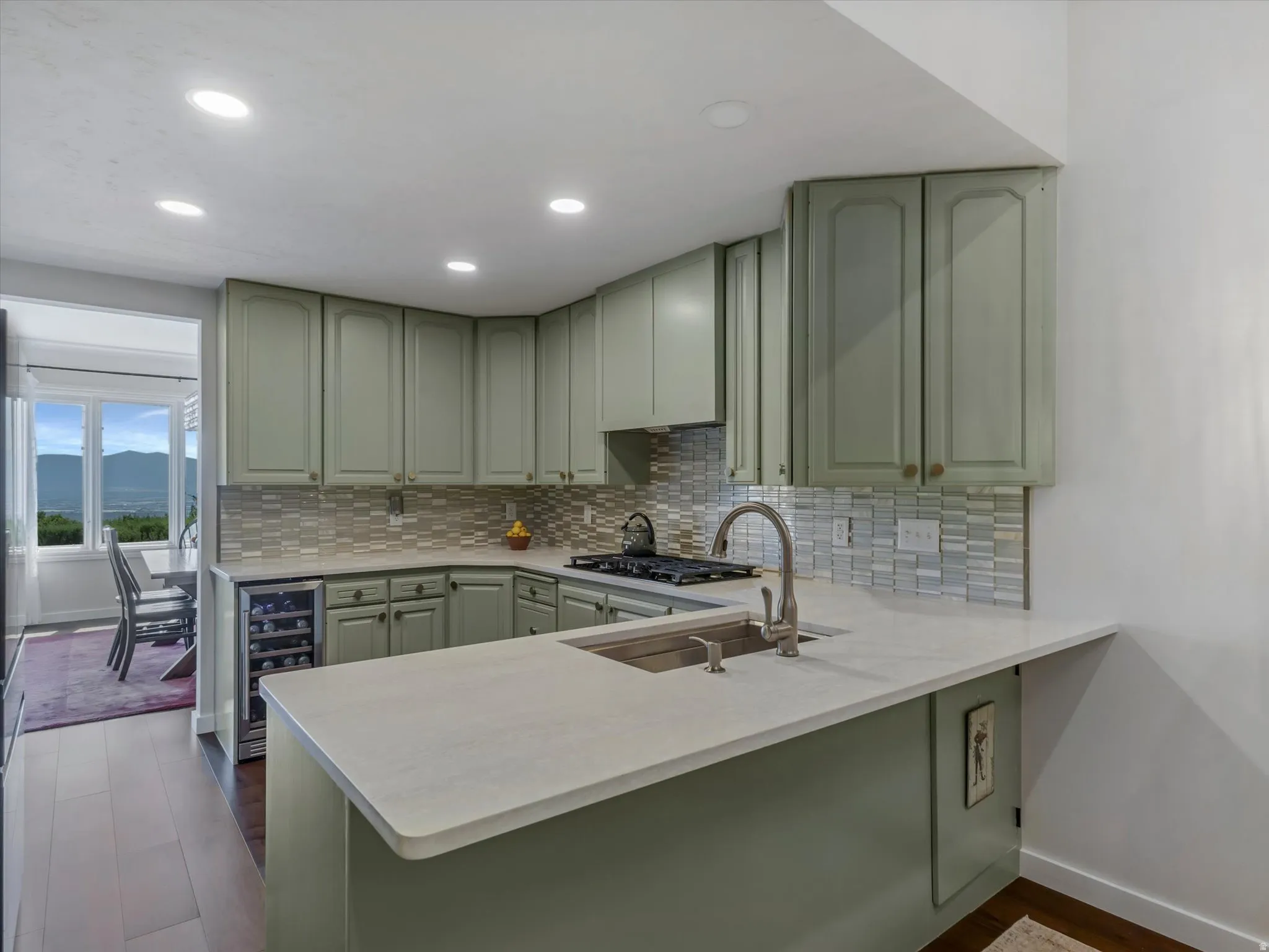 Kitchen featuring sage-toned cabinetry, light-toned countertops, a stainless steel sink with gooseneck faucet, a tile backsplash, and recessed lighting