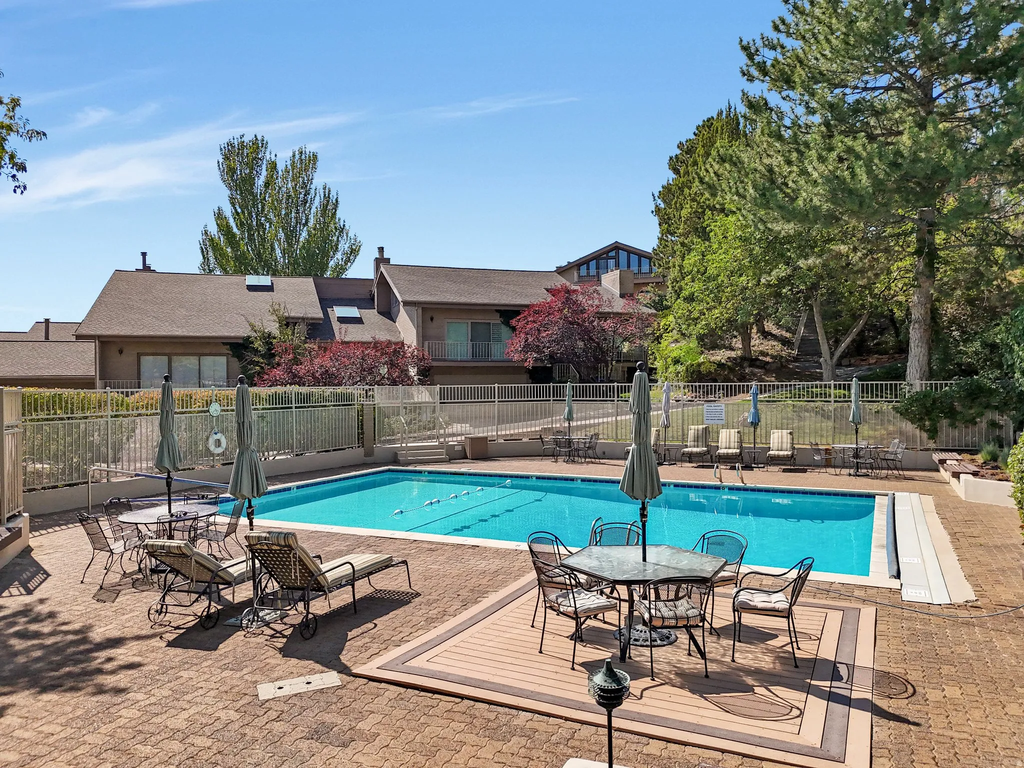 Swimming pool with a brick paver surround, integrated wood-finish decking, and perimeter fencing