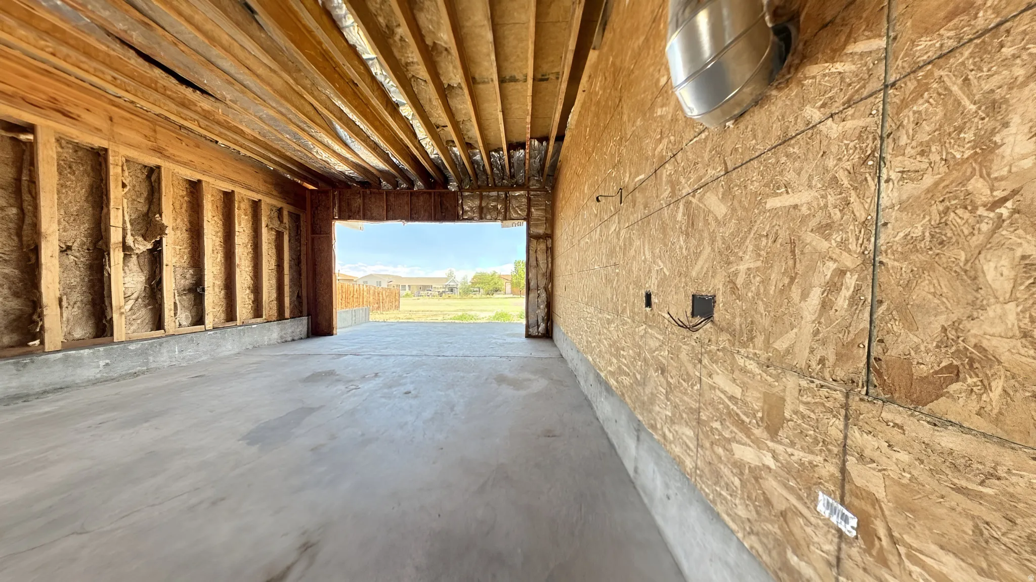 Unfinished interior space featuring exposed wood framing, oriented strand board walls, a concrete floor, and an open entryway