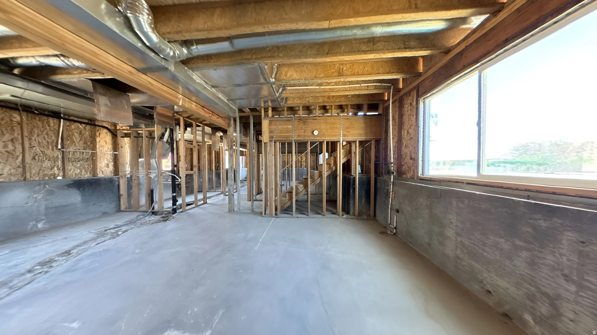 Unfinished interior space featuring exposed wood framing, concrete flooring, and a large window providing ample natural light