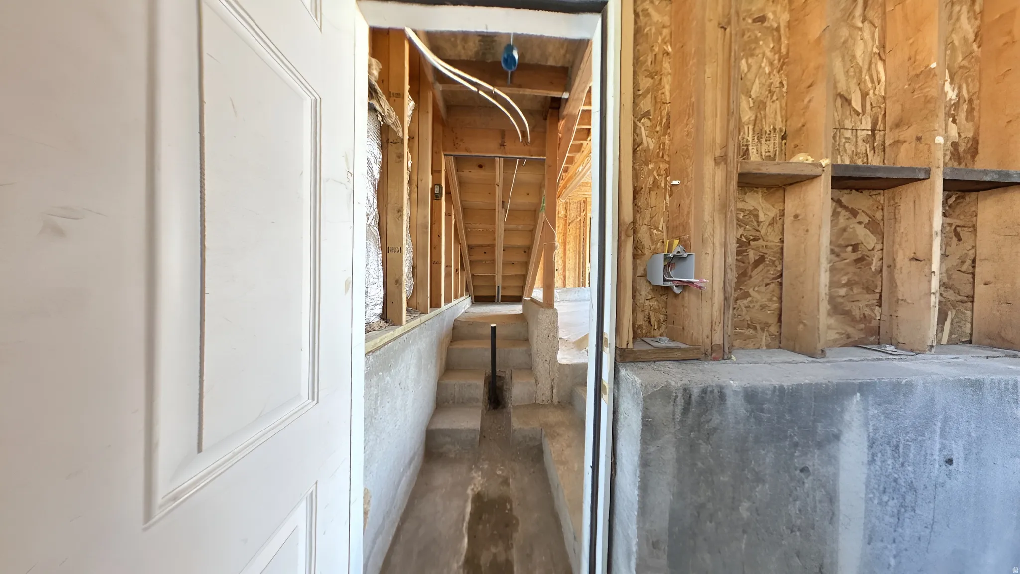 Unfinished basement featuring exposed wood framing, poured concrete walls, and concrete stairs